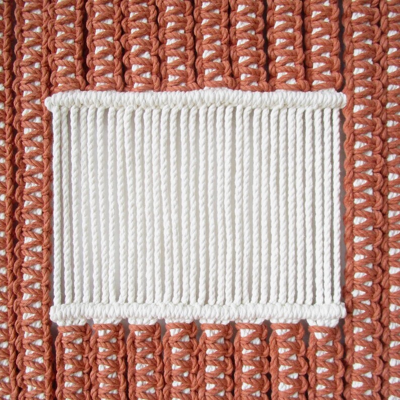 Puede incluir: Primer plano de un tapiz de macram&eacute; de pared con una secci&oacute;n rectangular blanca en el centro. El tapiz de pared est&aacute; hecho con cord&oacute;n marr&oacute;n y blanco.