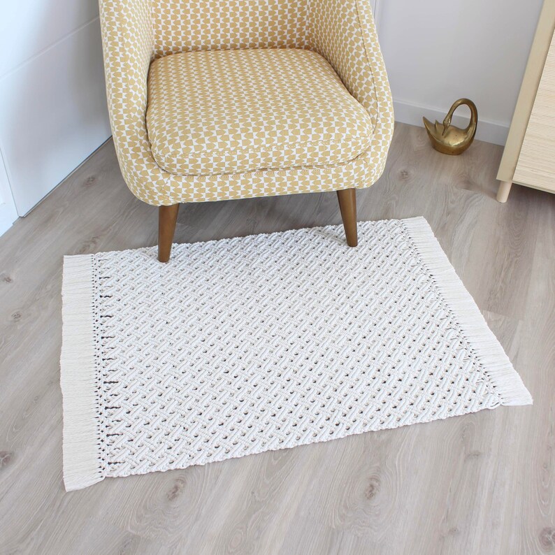 May include: A white woven rug with fringe edges, placed in front of a yellow patterned armchair with wooden legs.