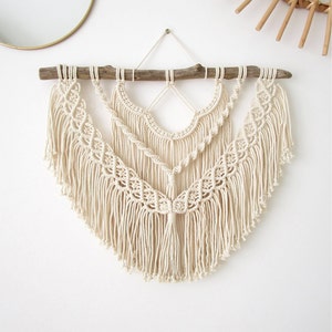 May include: A white macrame wall hanging with a wooden branch at the top and a fringe design.