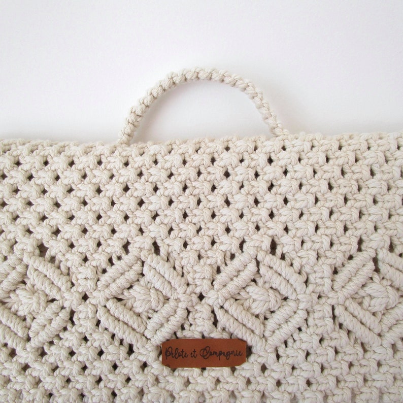 K&ouml;nnte beinhalten: Eine wei&szlig;e Makramee-Tasche mit einem braunen Lederanh&auml;nger, auf dem "Petite et Campagnarde" steht.