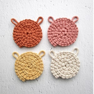 May include: Four crocheted pot holders in different colours: orange, pink, yellow, and white. Each pot holder has two loops for hanging.