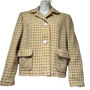 May include: A vintage beige jacket with a grid pattern in brown. The jacket features two front pockets, a collared neckline, and two white buttons. The jacket is a classic style.