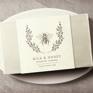 May include: A white bar of soap with a label that reads "Milk & Honey botanical company luxury hand soap" and features a black and white illustration of a bee inside a wreath of leaves.