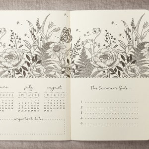 K&ouml;nnte beinhalten: Ein leeres Tagebuch mit einem floralen Design auf dem Umschlag. Das Tagebuch enth&auml;lt einen Kalender f&uuml;r Juni, Juli und August. Der Text "This Summer's Goals..." steht auf der rechten Seite.