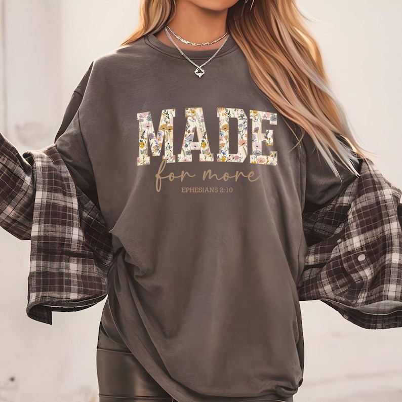 May include: A gray long-sleeve t-shirt with a floral print design that says "MADE for more EPHESIANS 2:10".