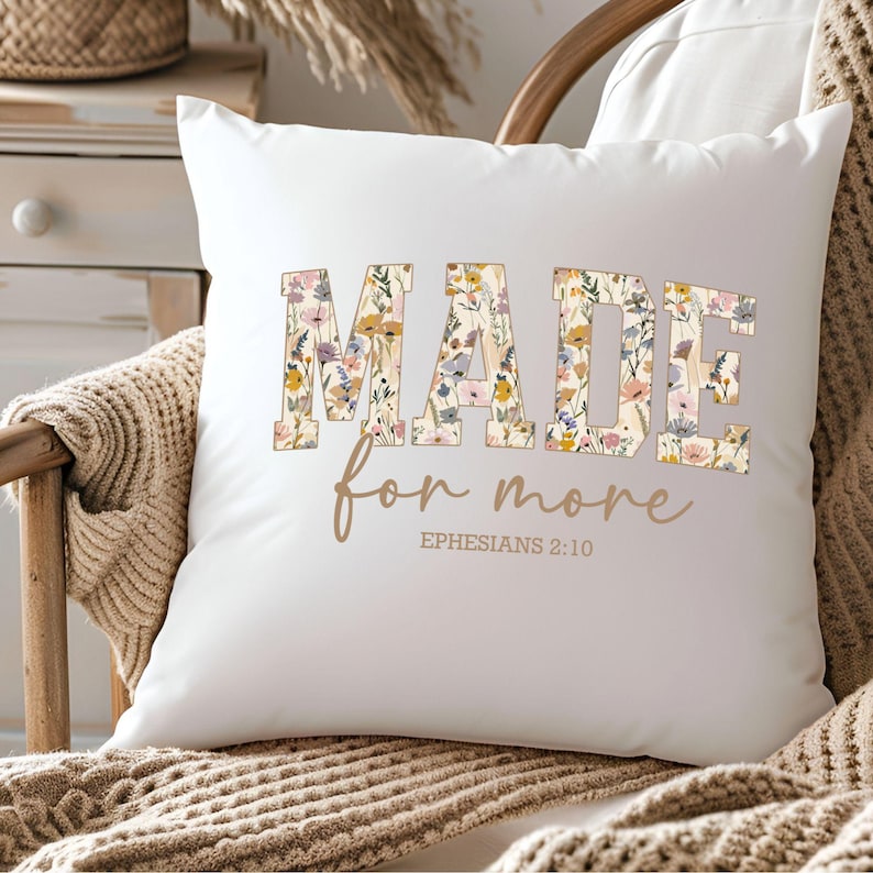 May include: White throw pillow with a floral design that spells out the word "MADE" with the text "for more" and "EPHESIANS 2:10" underneath.