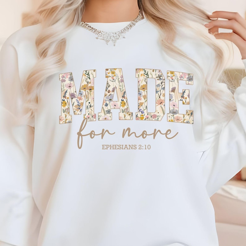 May include: White sweatshirt with a floral design spelling out the word "MADE" with the text "for more" and "EPHESIANS 2:10" underneath.