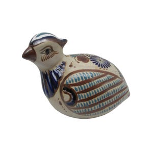 May include: A ceramic bird figurine with a cream-colored body, brown and blue patterned wings, and a brown beak. The bird has blue and white accents on its head and neck, and is a decorative item.