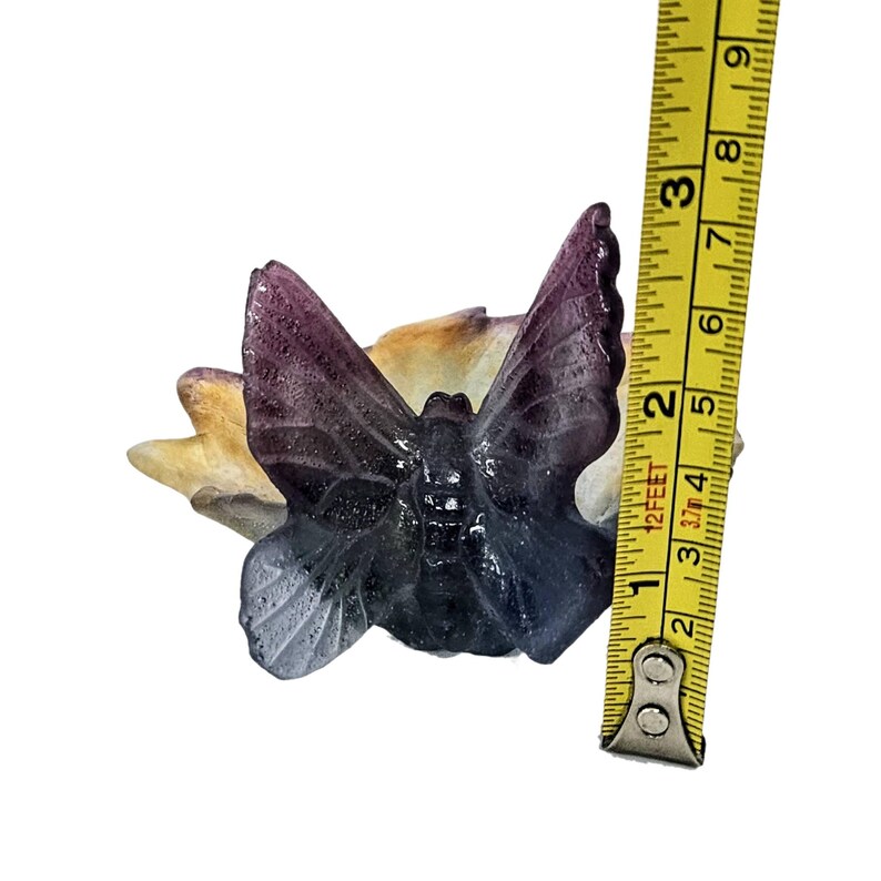 May include: A glass butterfly figurine with purple, blue, and white iridescent wings. The butterfly is sitting on a yellow and white flower base. The figurine is approximately 2 inches tall.