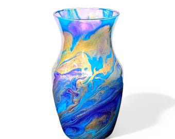 May include: A decorative glass vase with a unique, swirling paint design. The vase features a blend of blue, gold, purple, and teal colors. The vase has a wide base that tapers upwards to a narrower neck and flared rim.