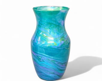 May include: A decorative glass vase with a swirling pattern of teal, blue, and green colors. The vase has a wide base that tapers to a narrower neck and flares out at the top. The glass has a glossy finish.