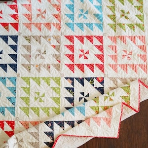 Puede incluir: Una colcha blanca con un diseño de patchwork que presenta varios patrones florales y formas geométricas en tonos de azul, verde, rosa y rojo. La colcha está doblada por la mitad y los bordes son visibles.