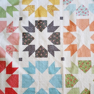 Peut inclure: Une courtepointe blanche avec un motif de patchwork présentant diverses couleurs et motifs. La courtepointe est composée de carrés et de triangles, avec un motif en forme d'étoile au centre. La courtepointe est réalisée avec une variété de tissus, notamment des imprimés floraux, des motifs géométriques et des couleurs unies.