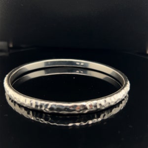 Puede incluir: Un brazalete de plata martillado. El brazalete es liso y brillante, con una textura martillada.