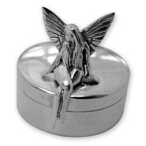 Könnte beinhalten: Silberfarbene Schmuckdose mit einer sitzenden Feenfigur auf dem Deckel. Die Fee hat detaillierte Flügel und langes, fließendes Haar. Die Dose ist rund und hat eine glatte, reflektierende Oberfläche.