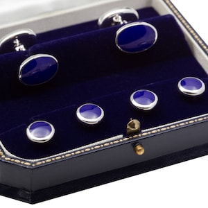 May include: A blue velvet box with a gold trim holds six silver cufflinks with blue enamel. The cufflinks are arranged in two rows of three.