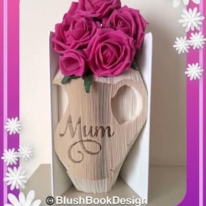 May include: A handmade paper art piece featuring a vase shape cut from book pages, with the word "Mum" cut out. The vase holds a bouquet of vibrant pink roses. The design is set against a white background with a pink and purple border.