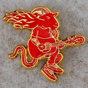 May include: A red and gold metal pin of a devil playing a guitar. The devil has horns, a tail, and wings.
