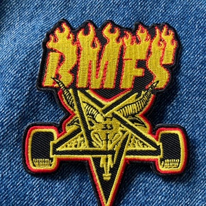 May include: A yellow and red embroidered patch with the word "BMES" in flames above a black pentagram with a goat's head inside. The pentagram has two yellow and black skateboard wheels on either side.