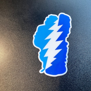 May include: A blue and white sticker with a lightning bolt design. The sticker is shaped like the state of Idaho.