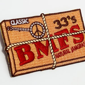 May include: Embroidered patch with a tan background and brown border. The patch features the text "CLASSIC" and "33's BMFS NATURAL JAMGRASS" in red and white. A banjo and peace sign are also included in the design, with a rope-like border.