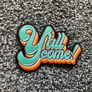 May include: A green, orange, and white embroidered patch with the text "Y'all come!" in a retro font style.