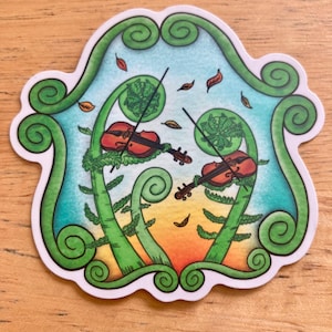 May include: A die-cut sticker featuring two brown violins being played by green fern fronds. The background shows a gradient from light blue to orange with small floating leaves. The entire scene is framed by a large, swirling green fern border.