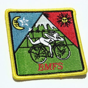 May include: Embroidered patch with a yellow border featuring a whimsical design. The patch depicts a person riding a bicycle, with a mountain, sun, moon, and stars. The text "BMFS" is at the bottom. The patch has a green, blue, and red color scheme.