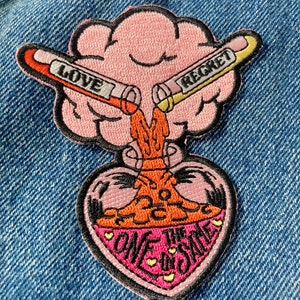 May include: Pink embroidered patch with a heart-shaped vial filled with orange liquid. Two test tubes labeled "Love" and "Regret" are pouring into the vial. The text "One the Same" is written on the heart.