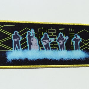 May include: A black and yellow embroidered patch featuring a silhouette of a band with musical instruments against a background of geometric shapes and a blue cloud effect.