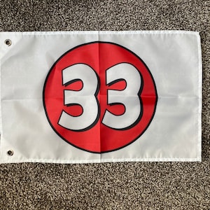 May include: White flag with a red circle containing the number 33 in white. The flag has two grommets.