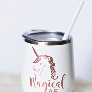 Puede incluir: Un vaso de acero inoxidable blanco con un unicornio dorado rosa y el texto "magical AF". El vaso tiene una tapa y una pajita blanca.