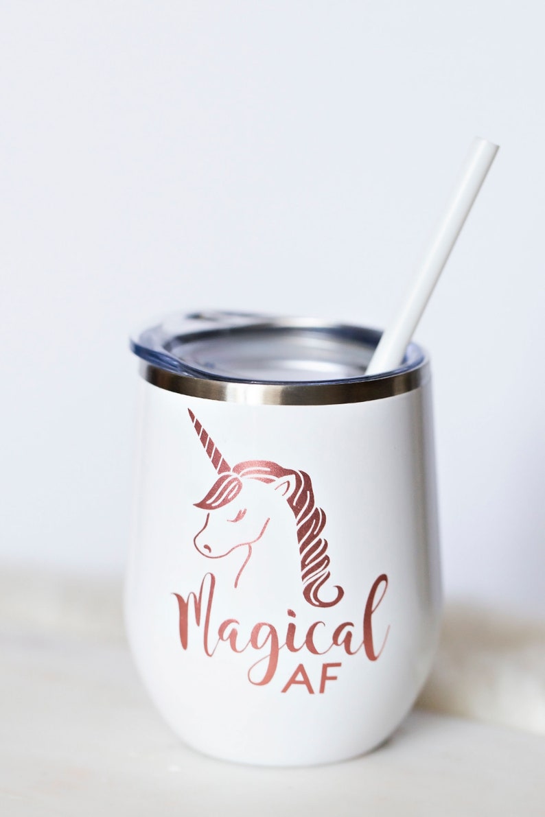 Puede incluir: Un vaso de acero inoxidable blanco con un unicornio dorado rosa y el texto "magical AF". El vaso tiene una tapa y una pajita blanca.