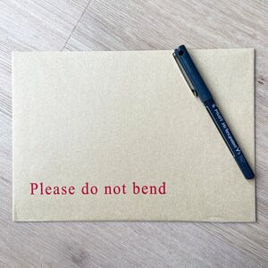 May include: A brown paper envelope with the words "Please do not bend" printed in red. A black pen is lying on top of the envelope.