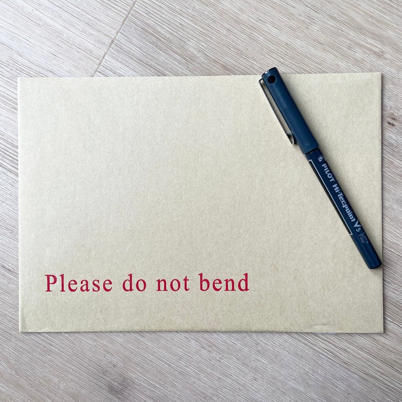 May include: A brown paper envelope with the words "Please do not bend" printed in red. A black pen is lying on top of the envelope.
