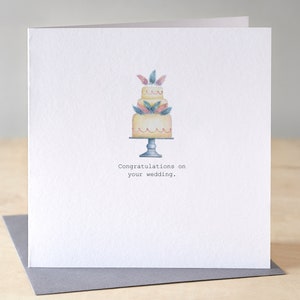 A Wedding Congratulations card with a hand painted 3 tiered cake on a stand. There are delicate little pink and blue feathers placed within each layer.