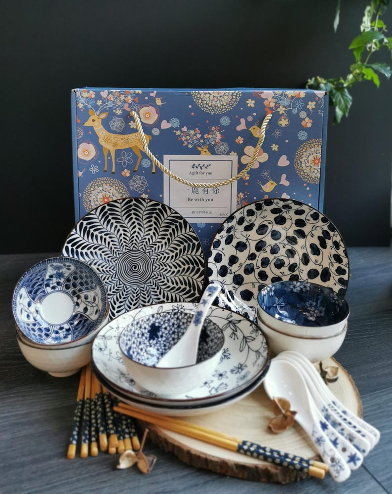 May include: A blue gift box with a deer and floral design contains a set of ceramic tableware. The set includes plates, bowls, spoons, and chopsticks with blue and white floral patterns. The text on the box reads "Gift for you" and "Be with you".
