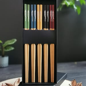 May include: Set of six pairs of chopsticks in a black box. The chopsticks are made of natural bamboo and have a fish design on the top. The chopsticks are available in six different colours: green, blue, yellow, black, red, and brown.