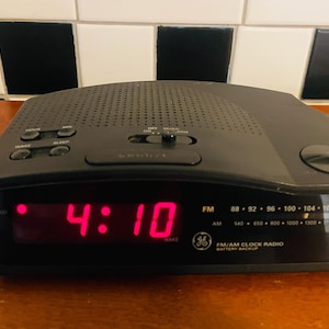 Könnte beinhalten: Schwarzes GE FM/AM-Radiowecker mit roter Digitalanzeige 4:10. Mit Tasten für Stunde, Minute, Schlummerfunktion und Sleep. Inklusive UKW-Frequenzoptionen und Batterie-Backup.
