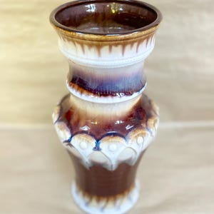 Peut inclure: Un vase décoratif en céramique avec une base évasée et un large sommet ouvert. Le vase présente une palette de couleurs marron, blanc et violet. Le design comprend une série de motifs festonnés blancs autour de la section centrale.