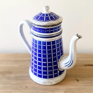 Peut inclure: Une cafetière cylindrique en émail arborant un motif à carreaux bleu et blanc. Elle est dotée d'un couvercle assorti avec un petit bouton, d'une anse incurvée et d'un bec verseur. La base et les bords du couvercle présentent des éclats.