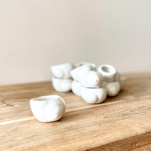 Peut inclure: Une collection de petits objets en céramique blanche en forme d'escargot. Une pièce individuelle est placée au premier plan, tandis qu'un groupe de plusieurs pièces identiques est disposé derrière, révélant leurs formes lisses et arrondies.