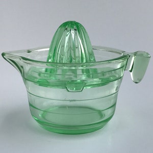 Può includere: Uno spremiagrumi in vetro verde con un estrattore a coste e una caraffa con manico.