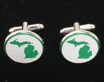 Peut inclure: Une paire de boutons de manchette en argent avec un fond blanc et un contour vert de l'état du Michigan.