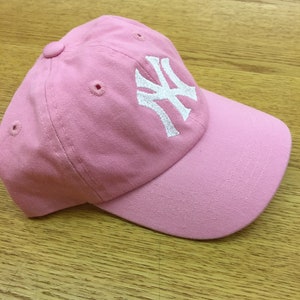 Peut inclure: Une casquette de baseball rose avec un logo brod&eacute; blanc des New York Yankees.