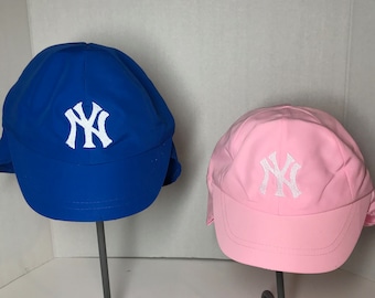Peut inclure: Deux casquettes de baseball avec un logo "NY" blanc. Une casquette est bleue et l'autre est rose.