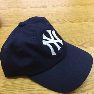 Peut inclure: Une casquette de baseball bleu marine avec un logo brod&eacute; blanc des New York Yankees.