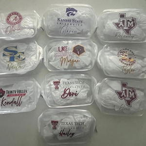 Puede incluir: Una colección de neceseres transparentes con cremallera, cada uno con un logotipo universitario diferente y un nombre personalizado en cursiva. Los logotipos incluyen Kansas State, Texas Tech, y otros. Los nombres incluyen Olivia, Gloria, Delaney, Naila, Morgan, Taylor, Kendall, Dori, Eleni y Hailey.