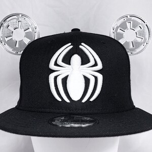 May include: Black and white baseball cap with a white spider design on the front. The cap has two silver Star Wars logos attached to the sides.
