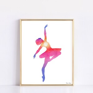 Ballerina art print featuring a silhouette painted in a double exposure style to be filled with a vibrant sunset. Watercolor print is displayed in a gold picture frame on a white background.